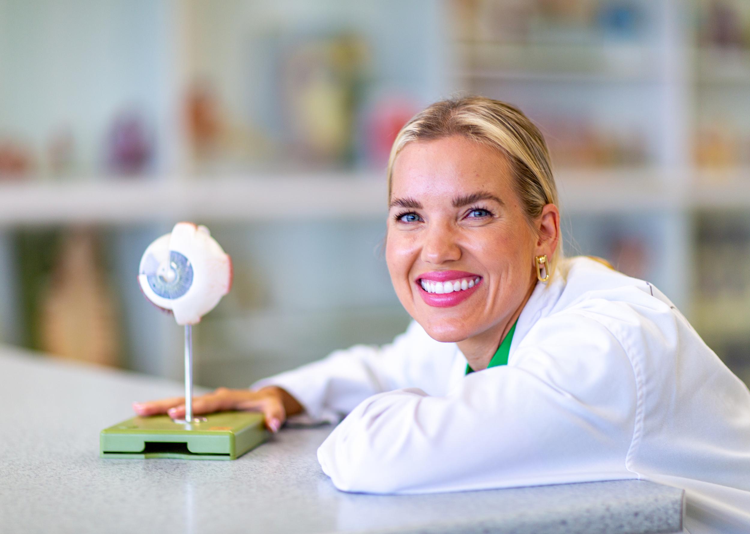 Woman leaning on counter in white coat with model eye