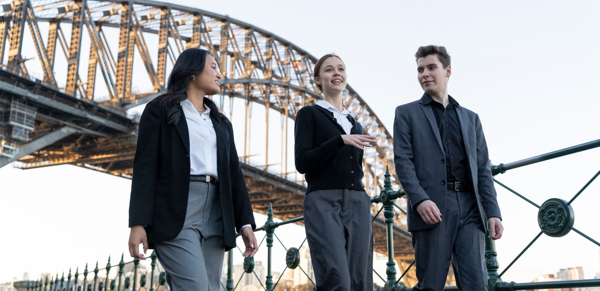 Two women and one man walking talking with bridge behind them