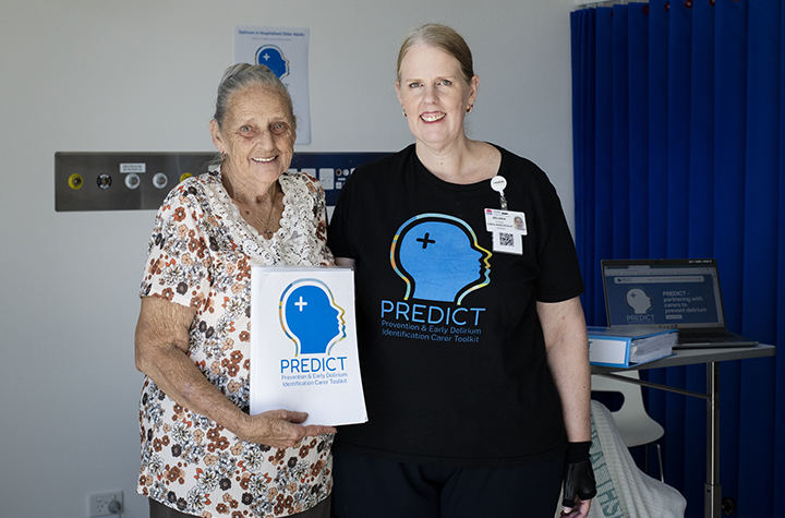 Two women in a hospital ward with PREDICT promotional material for delirium awareness