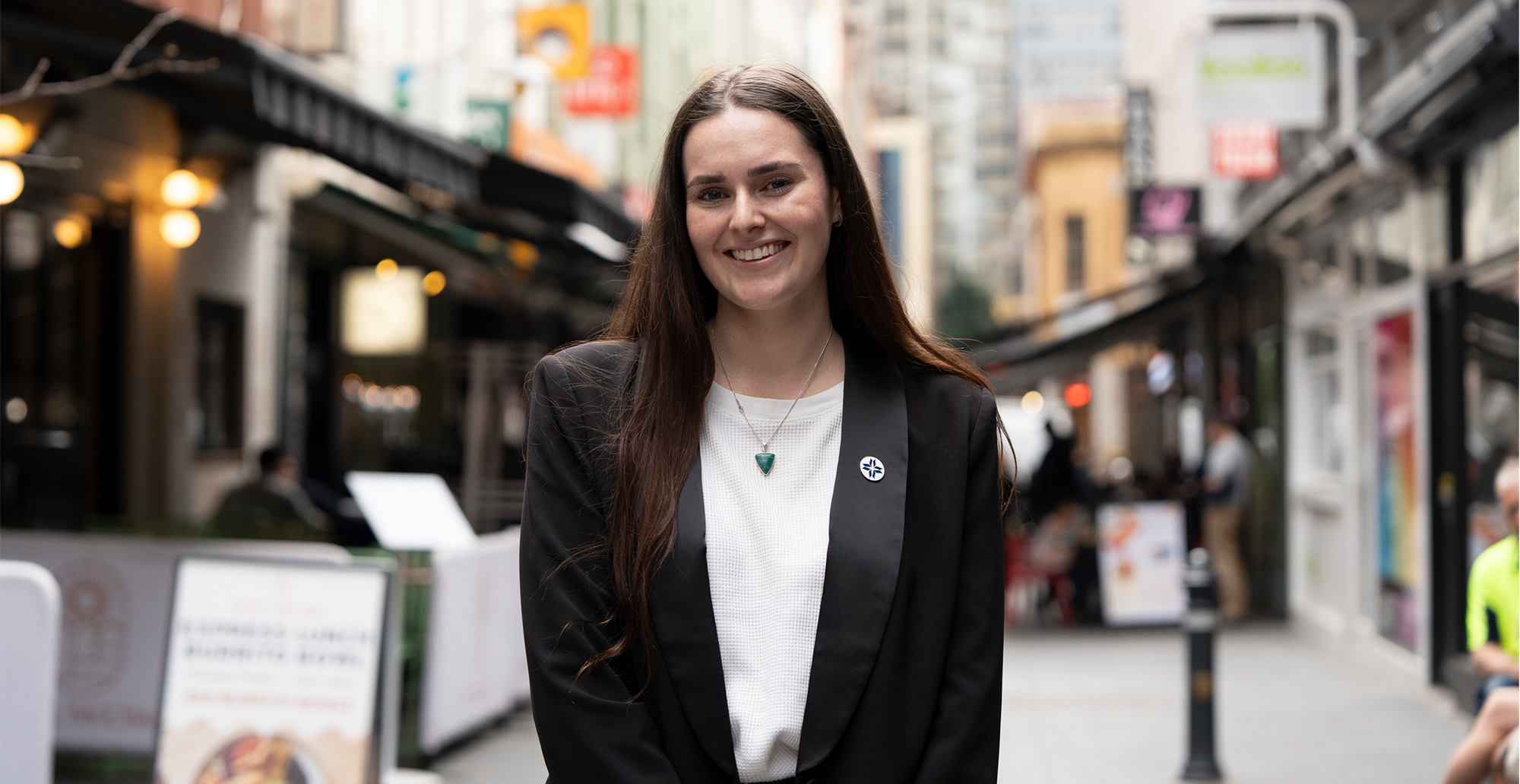 Woman in blazer standing in city street smiling at camera