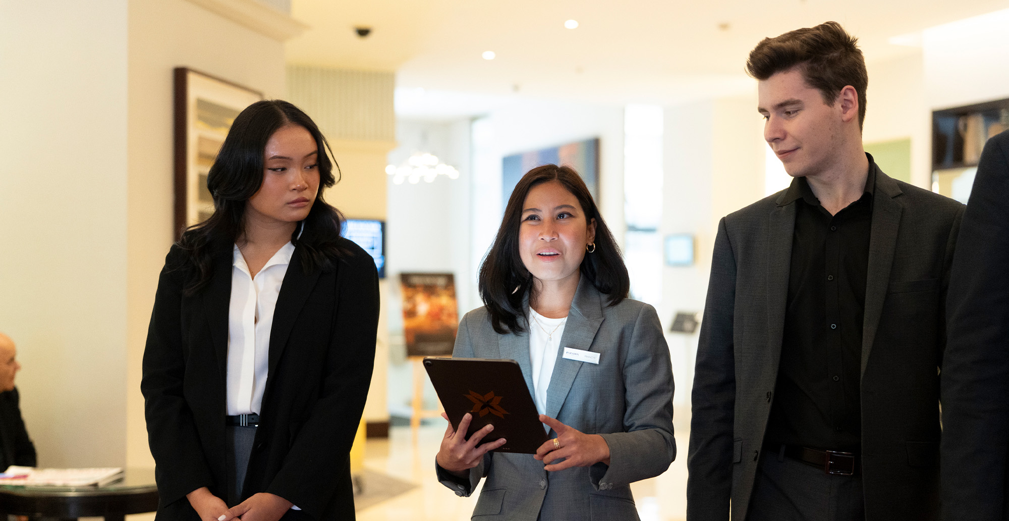Three people in suits walking in hotel lobby, middle person holding tablet