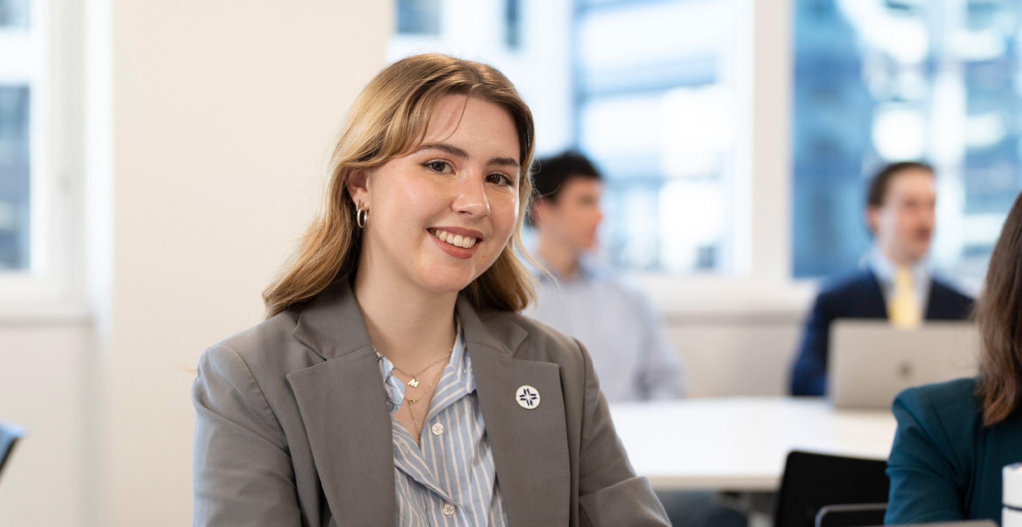 Woman in grey blazer smiling at camera in classroom setting