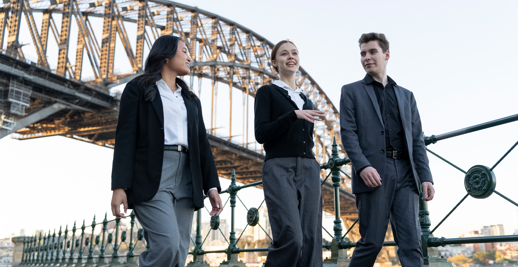 Two women and a man in business attire walking with Sydney Harbour Bridge in background