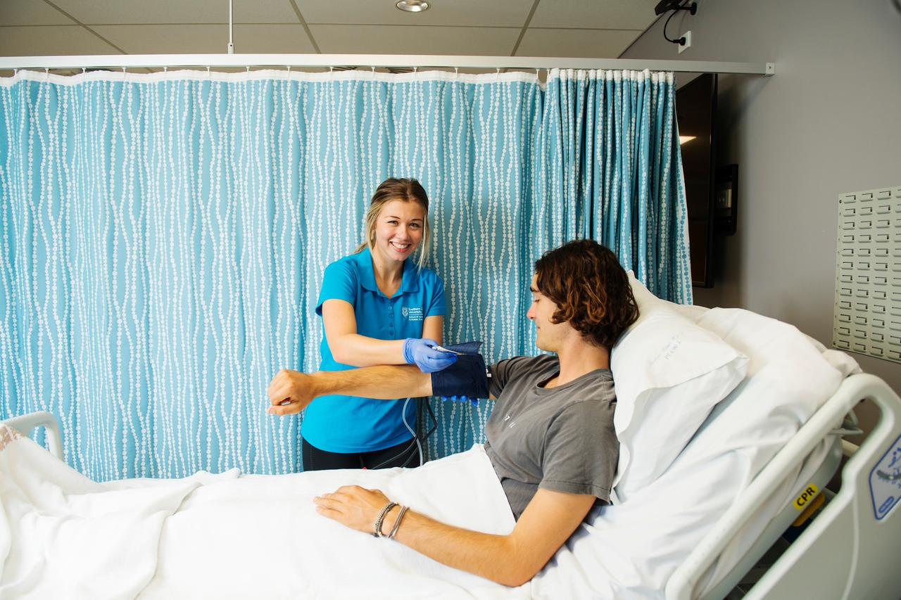 Student checking blood pressure of patient in hospital bed