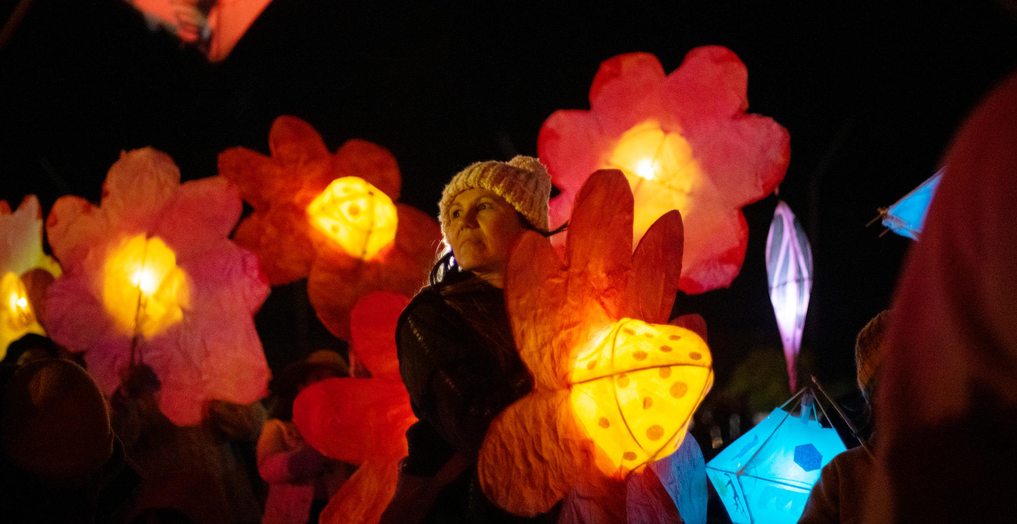 Woman in beanie holding lantern while other flower lanterns float around her